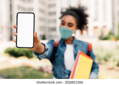 Black College Girl Showing Smartphone Empty Screen To Camera Advertising Educational Application For Students Standing Near University Building Outdoor. E-Learning App. Selective Focus On Phone