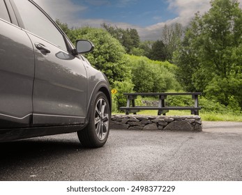 Black color car parked in a car park in a park close to a picnic area with table and bench, lush green forest in the background. Nobody. Outdoor activity. Cloudy sky - Powered by Shutterstock