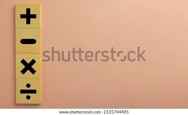 Black color of mathematical operations or Plus,\
minus, multiply, divide symbols on wooden cube over pink pastel\
background with copyspace  use for\
mathematic,education,background,school\
concept.