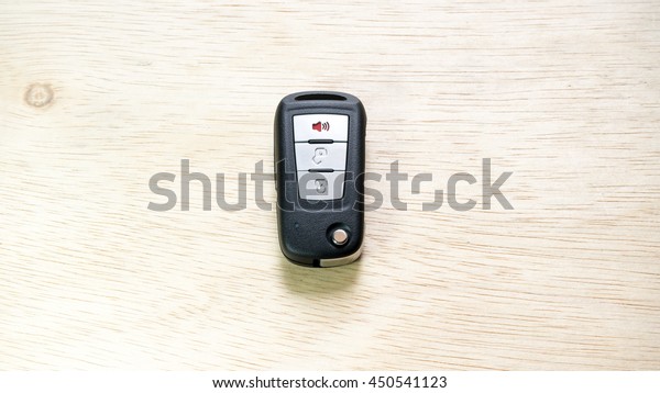 Black color modern car key door opener and keyless\
entry device with autolocking and alarm function on wooden surface.\
Concept of modern car security. Slightly de-focused and close-up\
shot. Copy space
