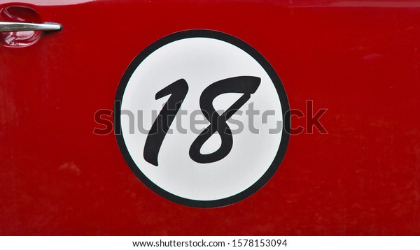 \
A black colored number in a\
white circle, on a red car door, showing the number eighteen\
(18)