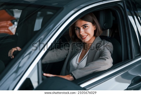 Black colored vehicle. Woman testing new car.\
Sitting indoors in modern\
automobile.