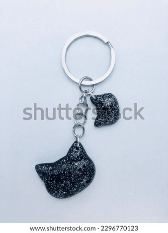 A black colour keytag on a white background. This keytag has two cat face shape keytags. The inside of the keytags have silver colour glitter powder. This keytag has silver colour keychain also.