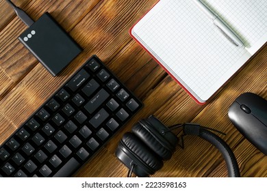 Black computer keyboard, external ssd, headphones, notepad with pen and computer mouse on a table made of wooden pine boards. Eco office. Periphery for gadgets and computer. Daylight - Shutterstock ID 2223598163