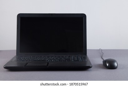 Black computer and mouse on gray table with empty screen.