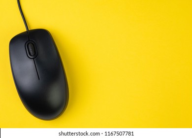 Black computer mouse with scroll wheel and cord on yellow table background with copy space, technology, advertising click through rate or internet and website concept.