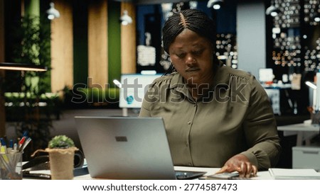 Black consultant proofreading a document before transcribing on notebook, handwritten notes on a text book at night time. Woman engaged in documenting important ideas from reports. Camera B.