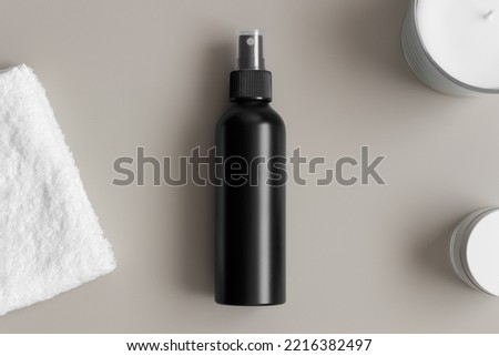 Black cosmetic spray bottle mockup with a towel on the beige table.