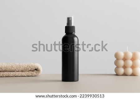 Black cosmetic spray bottle mockup with a candle and a towel on the beige table.