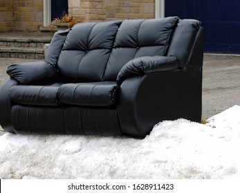 Black Couch Or Sofa On Snow At Curb. For Garbage Or Trash Pickup