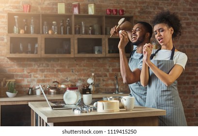 Black Couple Dancing And Singing Near Table With Food In Kitchen. Family Having Fun While Preparing Pastry