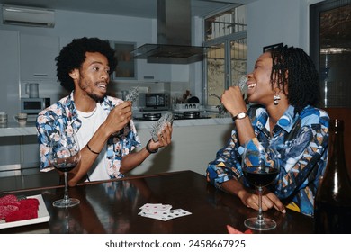 Black couple drinking wine and playing cards at home - Powered by Shutterstock