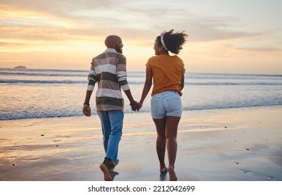 Black Couple, Holding Hands And On Beach With Sunset For Romance, Celebrate Relationship Or Holiday Together. Love, Happy Man And Woman Bare Feet, Relax Or Smile On Romantic Seaside Vacation Or Break