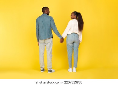 Black Couple Holding Hands Standing Back To Camera Posing Over Yellow Background. Studio Shot Of Unrecognizable African American Spouses. Marriage And Love Concept. Full Length - Shutterstock ID 2207313983