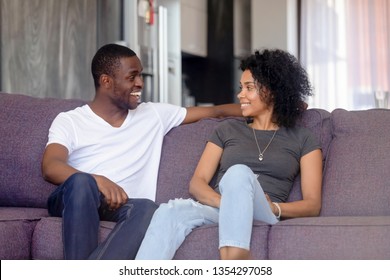 Black Couple Or Just Friends Sitting On Sofa In Living Room Communicating Talking At Home Spouses Looking At Each Other Smiling Laughing Chatting Planning Enjoy Time Together Love Flirt Dating Concept