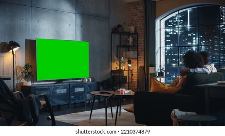 Black Couple In Love Sitting on a Couch, Watching Green Screen Chroma Key TV in Modern Loft Apartment. Boyfriend and Girlfriend Spend Time Together at Home as a Family. Back View. - Powered by Shutterstock