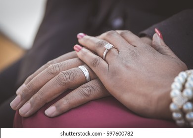 Black couple sitting holding hands with woman's hand on top of man's hand with wedding rings on closeup