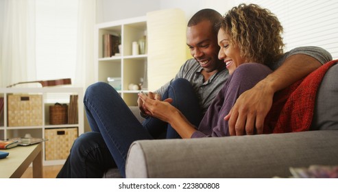 Black Couple Using Smartphone Together On Couch