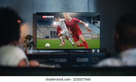 Black Couple Watches Professional Soccer Match on TV, Sitting on a Couch at Home in the Evening. Boyfriend and Girlfriend Football Fans Watch Sports. Back View Out of Focus Close Up Shot at Night. - Shutterstock ID 2210377645