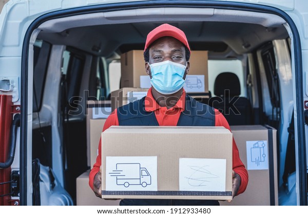 Black courier man delivering\
package in front of cargo truck wearing safety mask - Focus on\
face
