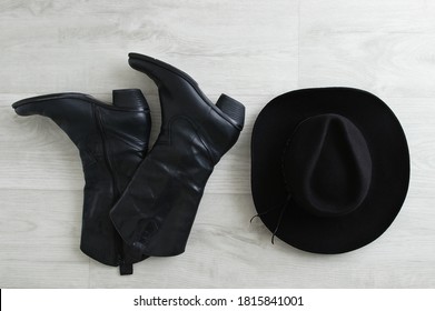 Black Cowboy Boots And Black Hat On A Gray Wooden Background. View From Above.