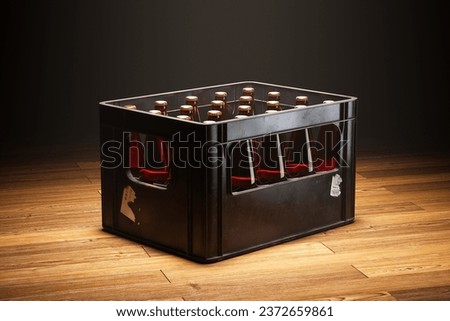 A black crate full of beer bottles standing in a spotlight on a wooden floor.