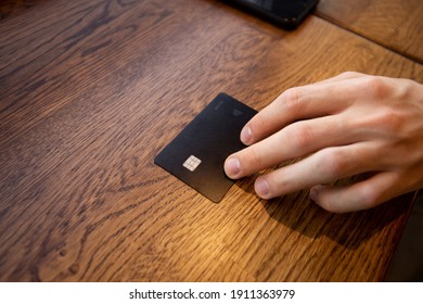 Black Credit Card Close Up. Male Hand Gives A Card To Pay Off The Bill. You Can Buy Anything Concept. Man's Hand Touching Card By Fingers. Keep Your Personal Data Safe From Scammers