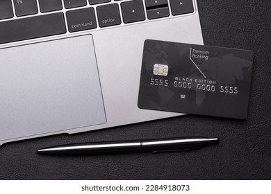 Black credit card on office table with laptop and pen. Flat lay. Premium banking concept