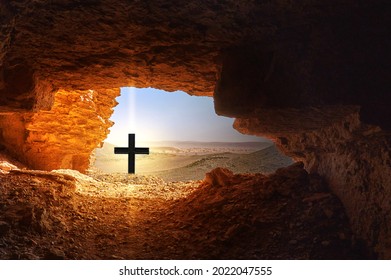 Black Cross With Bright Light In Front Of Dark Cave In The Dry Hostile Desert With Boulders