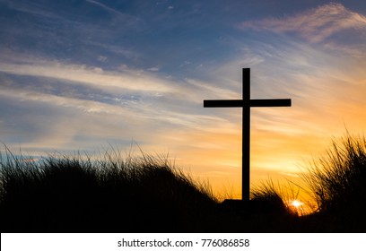 Black cross on a hill as the sunsets behind it.