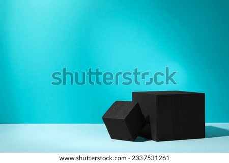 Black cubes on light table against turquoise background, space for text. Stylish presentation for product