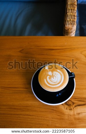 black cup of cappuccino on wooden background with beautiful latte art. morning routine, spending time in cafe. top view.