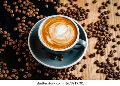 Black Cup Of Coffee On The Black And Brown Table Among Spilled Roasted Coffee Beans. Cappuccino With Cofee Art In The Cafe.