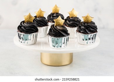 Black Cupcakes Decorated With A Gold Star On A Cake Stand