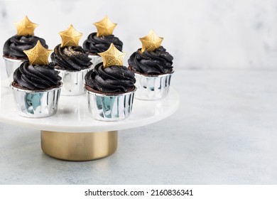 Black Cupcakes Decorated With A Gold Star On A Cake Stand