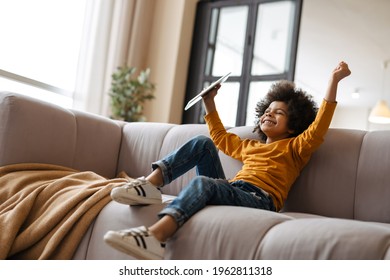 Black curly boy making fun and using tablet computer while sitting on sofa at home - Powered by Shutterstock