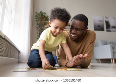 Black Dad Little Son Collect Jigsaw Puzzle Put Together Pieces On Warm Floor In Living Room. Leisure Activity Have Fun At Home, Logical Reasoning Ability, Develop Solving And Fine Motor Skill Concept