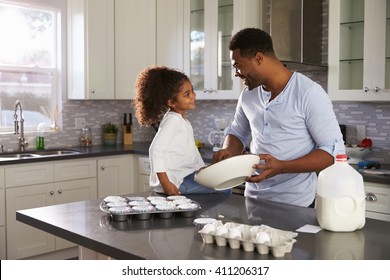 Black dad and young daughter look at each other while baking