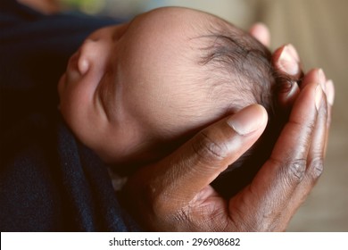 Black Daddy Holding Newborn Baby's Head In His Hands. Soft Focus.