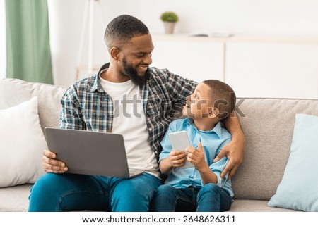 Black Daddy And Son Using Laptop And Phone At Home