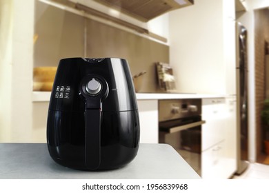 a black deep fryer or oil free fryer , air fryer appliance, is on the white marble table in the nice interior design kitchen of the house during the cooking dinner for family member in Christmas party