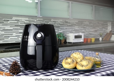 a black deep fryer or oil free fryer , air fryer appliance, and a dish of homemade bagel breads are on the table in the nice modern design kitchen for a breakfast