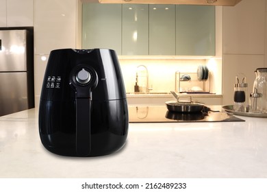 a black deep fryer or oil free fryer , air fryer appliance, is on white marble table in nice interior design kitchen dinning room of house during cooking dinner for family member in Christmas party