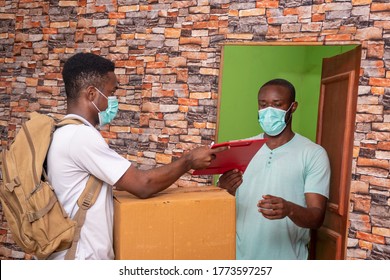 Black Delivery Worker Delivering A Package To A Customer, Both Wearing A Face Mask, Handing Over Manifest To Client