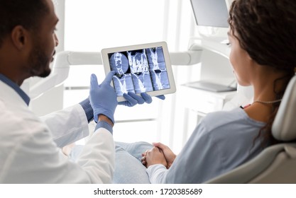 Black Dentist And Female Patient Looking At Xray Picture On Digital Screen At Clinic