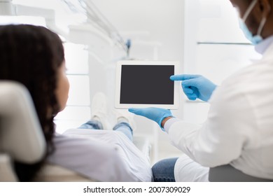 Black Dentist Showing Digital Tablet With Blank Screen To Female Patient During Check Up In Modern Stomatological Clinic, Demonstrating Dental Treatment Result Or Teeth X-Ray On Modern Gadget, Mockup