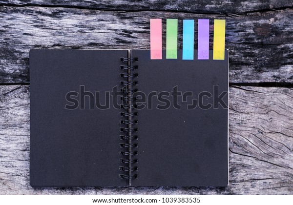 Black diary with colored tabs on wooden\
background. Five colorful bookmarks with notebook, closeup of color\
tabs for bookmarks, Different colorful sticky paper tag label. Case\
study concept.