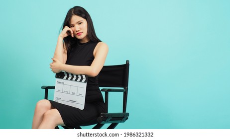 Black director chair and Asian woman is sit on it.She hold clapperboard on green or Tiffany Blue background.