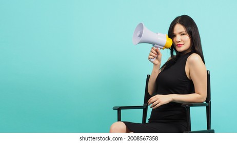 Black director chair and Asian woman is hold megaphone and sitting on it.It put green mint color or Tiffany Blue background.