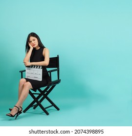 Black director chair and Asian woman is sitting and hold movie clapper board on mint green or Tiffany Blue background.